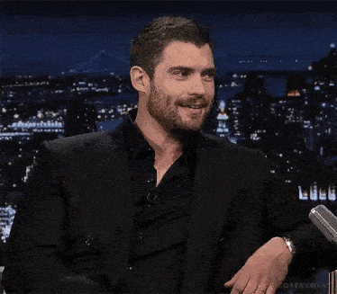 a man with a beard is wearing a black suit and black shirt .