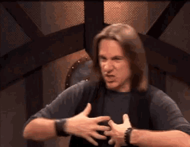 a man with long hair is making a funny face with his hands on his chest