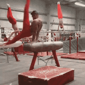 a gymnast is doing a trick on a pommel horse in a gym