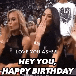two women are sitting in the stands at a basketball game and one is blowing a kiss .