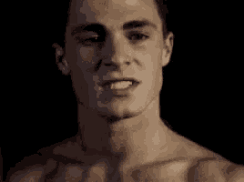 a close up of a shirtless man 's face in a dark room .