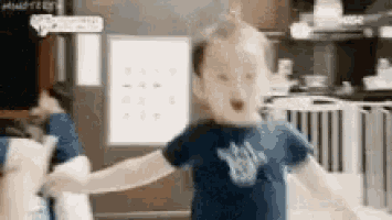 a little boy in a blue shirt is standing in a kitchen