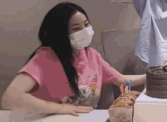 a woman wearing a mask is sitting at a table with a cake