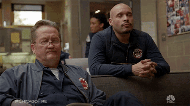 two men are sitting on a couch and one has a jacket that says chicago fire on it