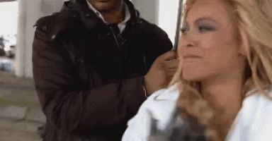 a woman with blonde hair is getting her hair done by a man in a black jacket .
