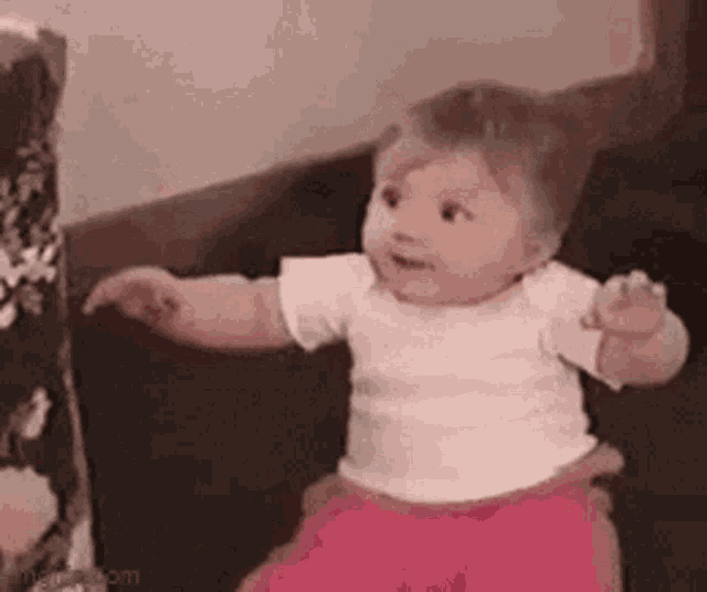 a baby girl is sitting on a couch with her arms outstretched .
