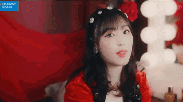 a girl in a red dress is sitting in front of a mirror and looking at the camera .