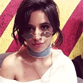 a woman wearing a choker and sunglasses is sitting in front of a striped wall .