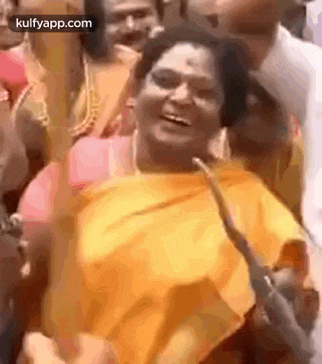 a woman in a yellow saree is laughing in a crowd .