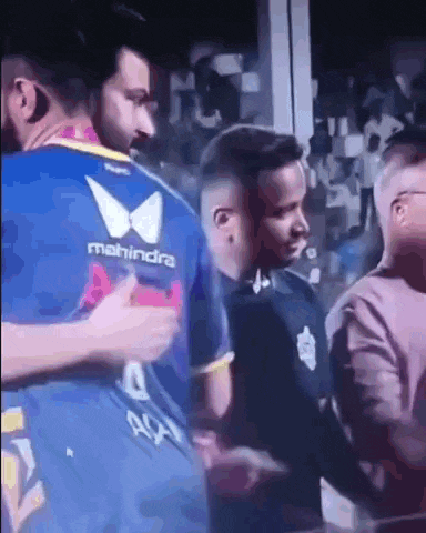 a group of men are standing next to each other in a crowd . one of the men is wearing a mahindra jersey .