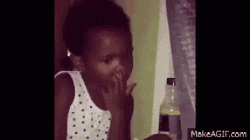 a young girl is covering her mouth with her hand while sitting at a table .