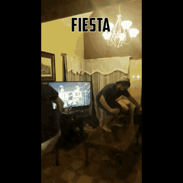 a man is jumping on a table in front of a television with the word fiesta above him