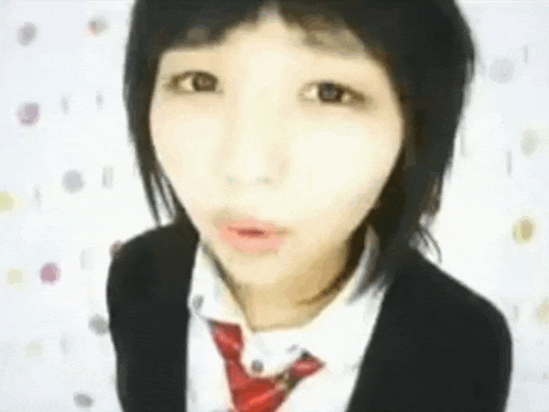a girl wearing a black jacket and a red tie looks at the camera .