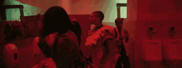 a group of people are standing in a bathroom in a dark room with red lights .