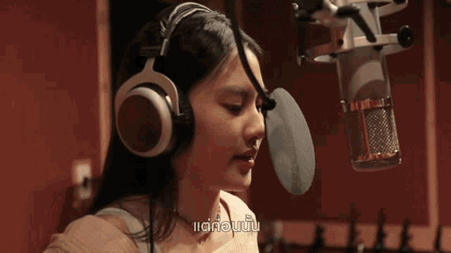 a woman wearing headphones is singing into a microphone with a foreign language subtitle
