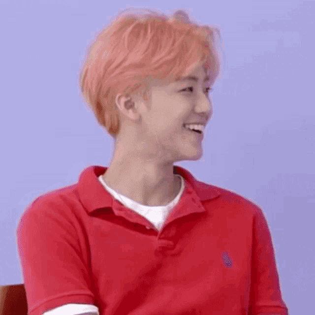 a man with pink hair is wearing a red polo shirt .