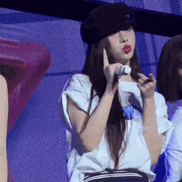 a woman wearing a hat and a white shirt is holding a microphone and making a face .