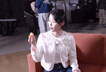 a woman in a white lace jacket is sitting on a couch holding a piece of food in her hand