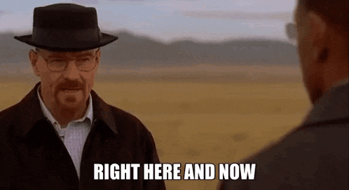 a man in a hat and glasses is talking to another man in a field and says `` right here and now '' .