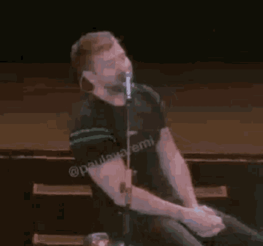 a man in a black shirt is singing into a microphone while sitting on a stage .