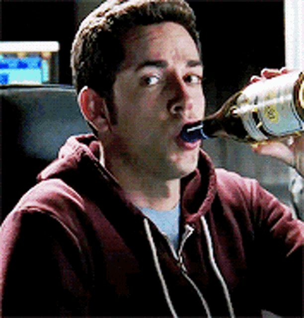 a man in a red hoodie is drinking from a bottle with a blue label