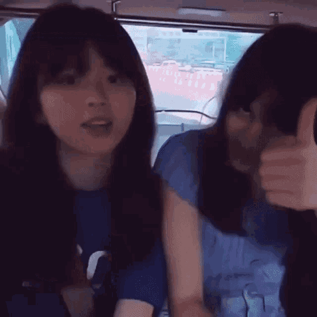 two girls are giving each other a thumbs up while sitting in a car .