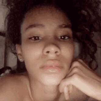a young woman with curly hair is taking a selfie with her hand on her face .