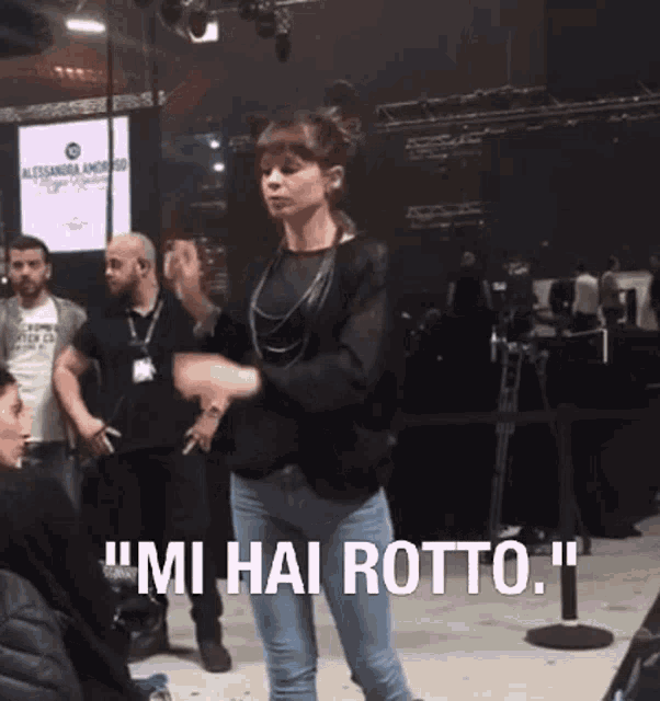 a woman is dancing in front of a crowd with the words " mi hai rotto " behind her .
