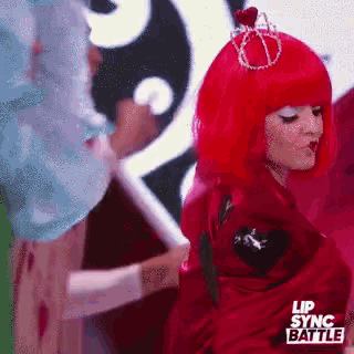 a woman in a red wig with a crown on her head is dancing on a stage .