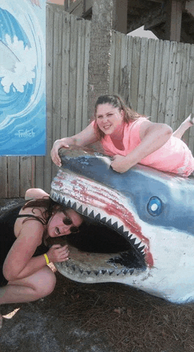 two women are posing for a picture with a shark statue in the background