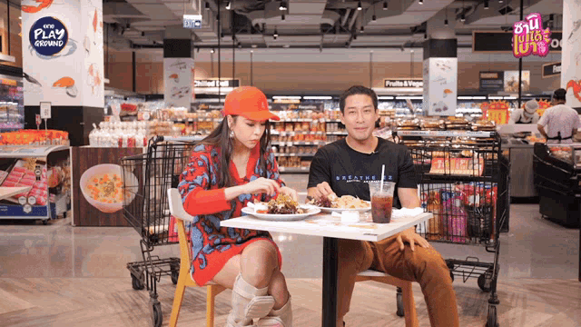 a man and a woman sit at a table in a grocery store with a sign that says play growing