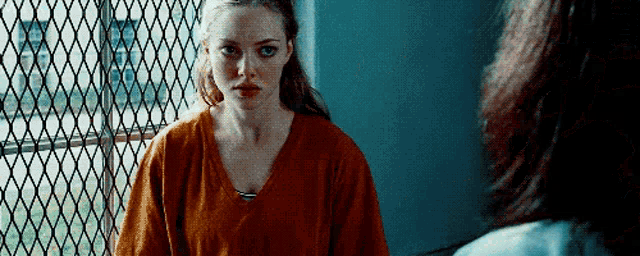 a woman in an orange shirt is standing in front of a chain link fence talking to another woman .