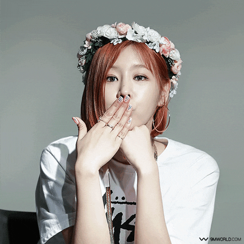 a woman wearing a flower crown covering her mouth with her hands