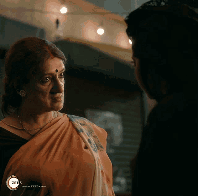 a woman in an orange saree stands next to a man in a black shirt with a zee5 logo in the corner