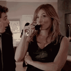 a woman is drinking a glass of wine while a man looks on .