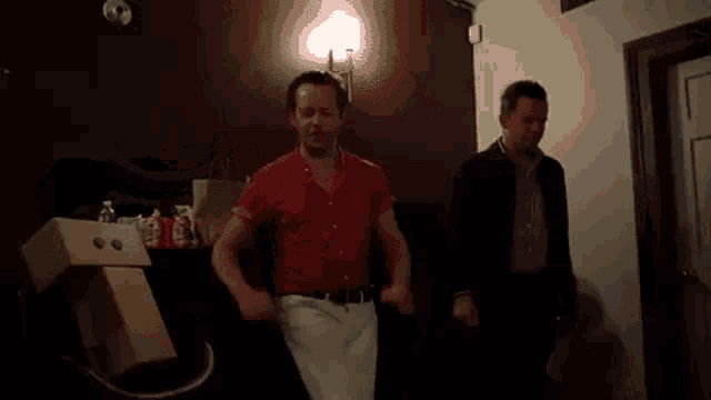 a man in a red shirt is dancing with another man in a dark room