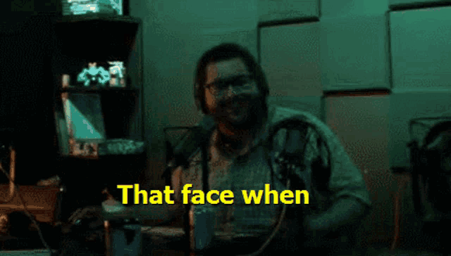 a man sitting in front of a microphone with the words " that face when " behind him