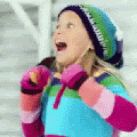 a little girl wearing a hat , mittens and a sweater is standing in the snow .