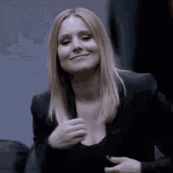 a woman in a black jacket is smiling and holding her breasts .