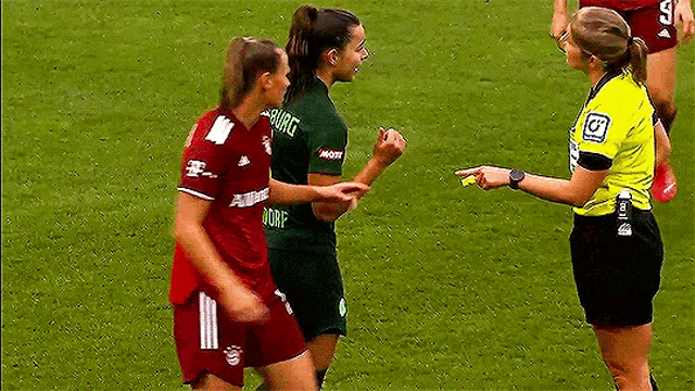 a referee is talking to two female soccer players one of whom is wearing a shirt that says dorf