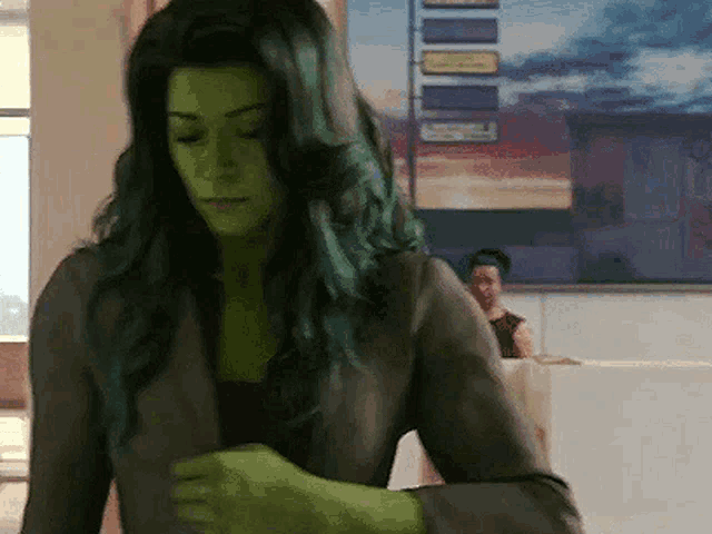 a woman with green hair is standing in a room with a painting on the wall .