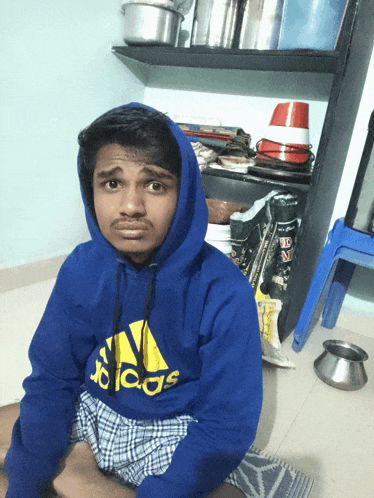 a young man wearing a blue adidas sweatshirt sits on the floor
