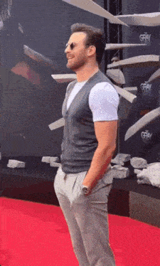 a man is standing on a red carpet with his hands in his pockets