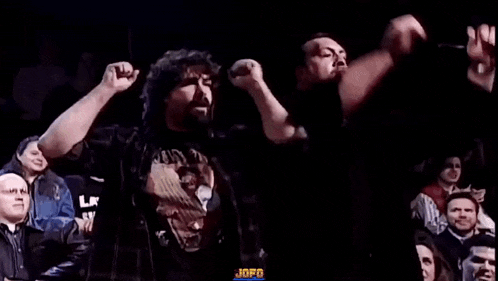 a man with a beard is standing in front of a crowd of people with his arms in the air .