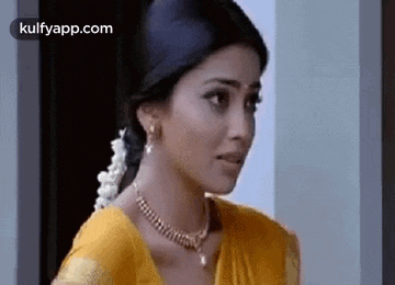 a woman in a yellow saree and a gold necklace is standing in front of a door .