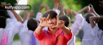 a man in a red shirt is making a frame with his hands in front of a group of children .
