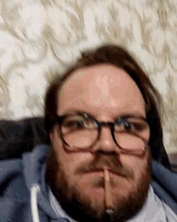 a man with glasses and a beard is smoking a cigarette in his mouth