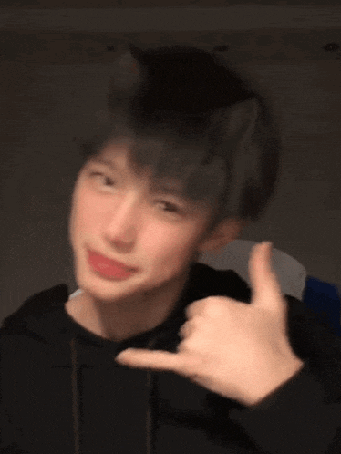 a young man with cat ears on his head is making a hand gesture .