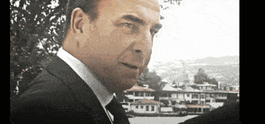 a man in a suit and tie is standing in front of a body of water