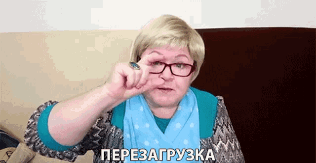 a woman wearing glasses and a blue scarf is making a funny face with her finger in her nose .